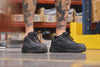 Still shot of the BRUNT 4 inch lightweight comp toe work sneaker in black on the job in warehouse with the background activity in motion